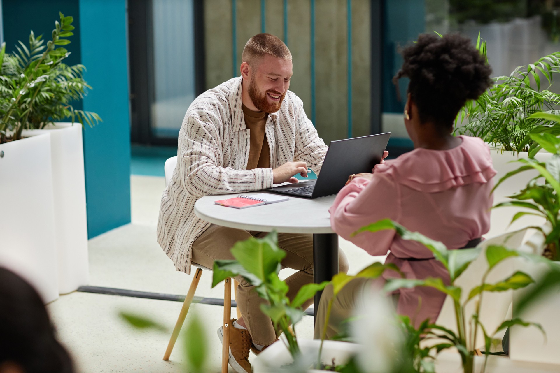 Smiling Man Using Laptop Sitting at Table with Female Colleague in Coworking Space